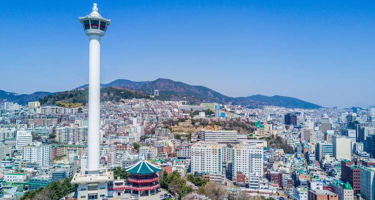 Aerial day view of Busan Tower rising above the dense urban landscape and surrounding hills.