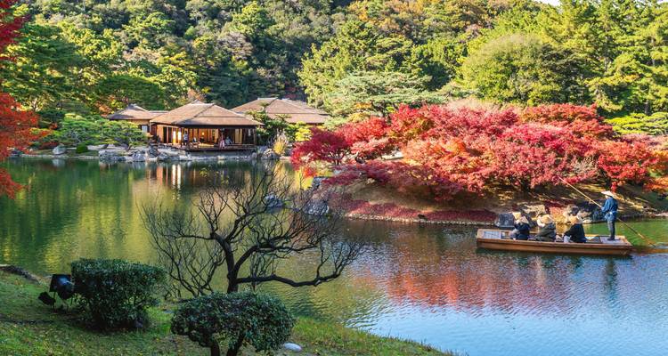 Boat glides across serene pond amid vibrant autumn foliage in a traditional Japanese garden.