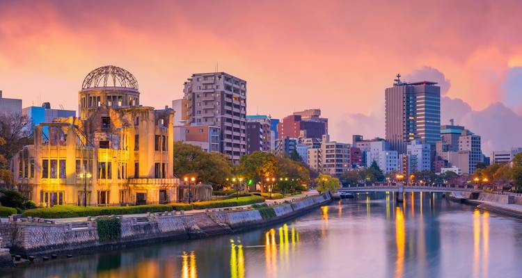 Evening view of Hiroshima skyline with the Atomic Bomb Dome beside a reflective river.