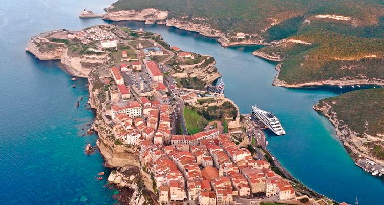 Vue aérienne de la ville de Bonifacio perchée sur les falaises avec des eaux turquoise et des yachts.