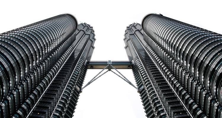Looking up at the twin Petronas Towers connected by the skybridge against a white sky.