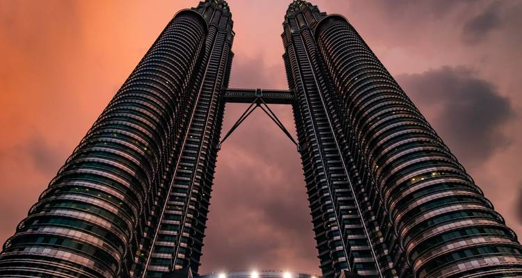 Dramatic low-angle shot of the Petronas Twin Towers piercing a fiery sunset sky.