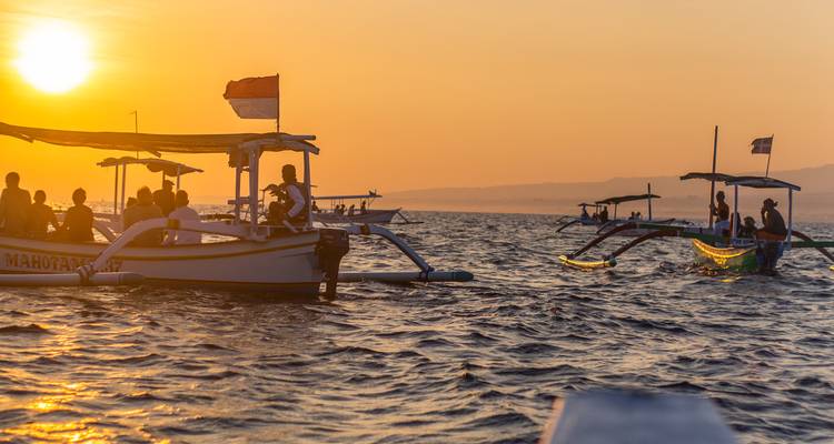 Botes tradicionales con estabilizadores en el mar al amanecer con pasajeros observando delfines frente a la costa de Bali.