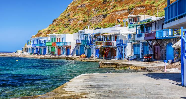 Rangée de maisons balnéaires aux couleurs vives avec balcons bordant un rivage calme et limpide sous un ciel bleu profond.