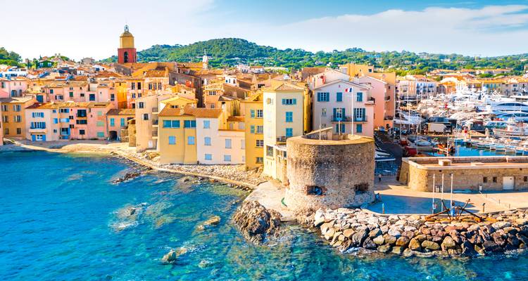 Des bâtiments colorés en bord de mer et une tour en pierre surplombant la mer Méditerranée turquoise à Saint-Tropez.