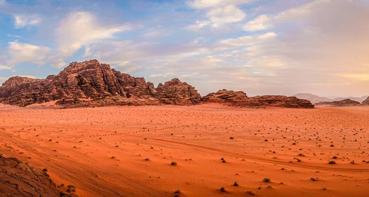Sweeping desert panorama of Wadi Rum with rugged sandstone mountains and orange sand under a dramatic sky.