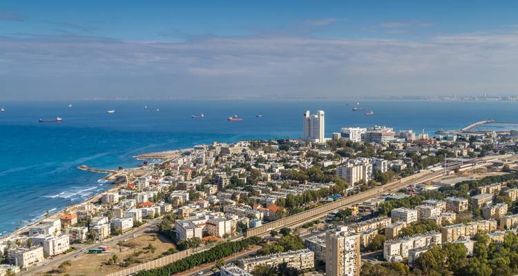 Coastal cityscape stretching along a blue bay with cargo ships offshore.