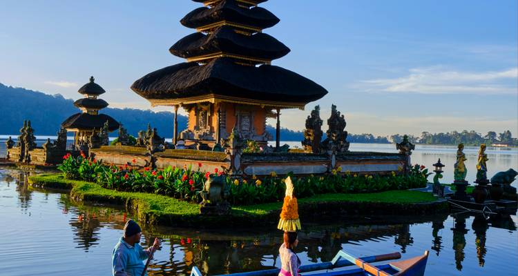 Close view of Ulun Danu Bratan temple complex with locals in traditional attire on a calm lake.