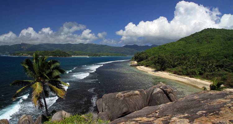 Un promontoire de forêt tropicale luxuriante rencontre un littoral corallien étroit avec des montagnes au loin.