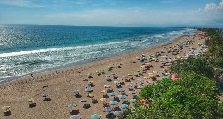 Wide sandy beach lined with colorful umbrellas and gentle waves rolling in from a sparkling sea.
