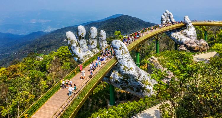 The famous Golden Bridge held by giant stone hands spans a lush mountain valley packed with visitors.