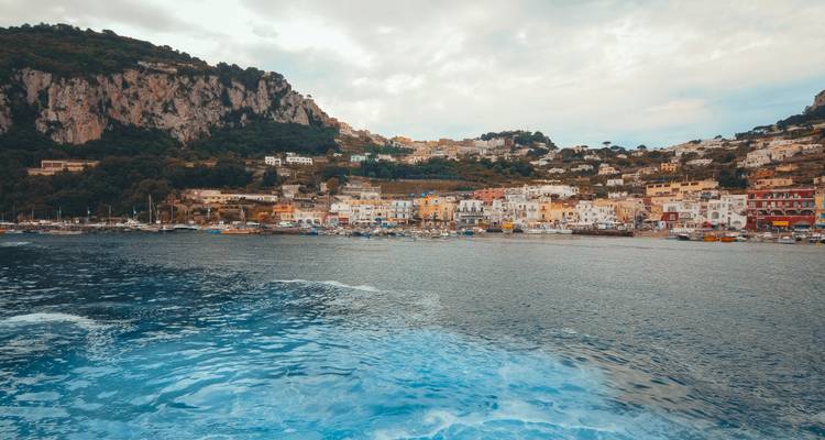 La ville côtière de Capri vue depuis la mer avec le sillage mousseux du bateau au premier plan.