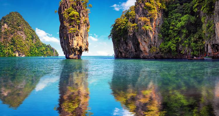 Iconic limestone karst of James Bond Island rising from mirror-like waters reflecting vivid cliffs and sky.