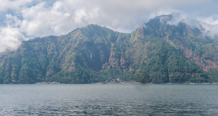 Forested mountains rising above a calm lake with light clouds clinging to the ridges.