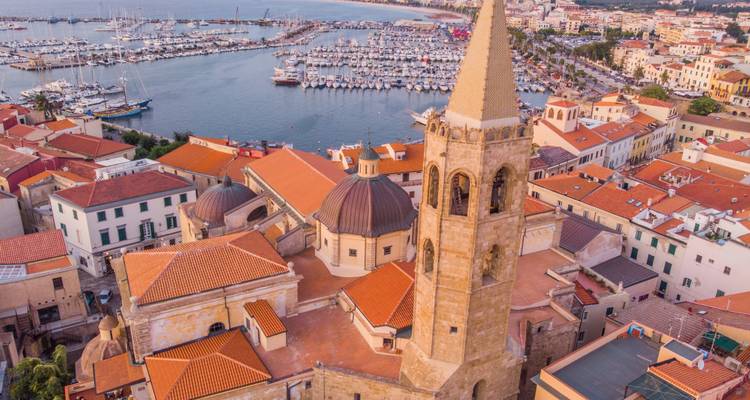 Vue aérienne du centre historique d'Alghero avec son haut campanile et sa marina s'étendant dans la baie.