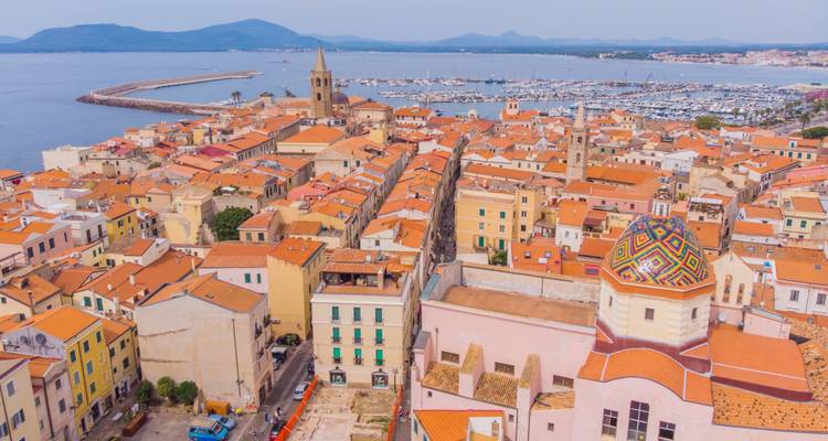 Aerial view of Alghero’s terracotta rooftops, cathedral and marina on the Sardinian coast.