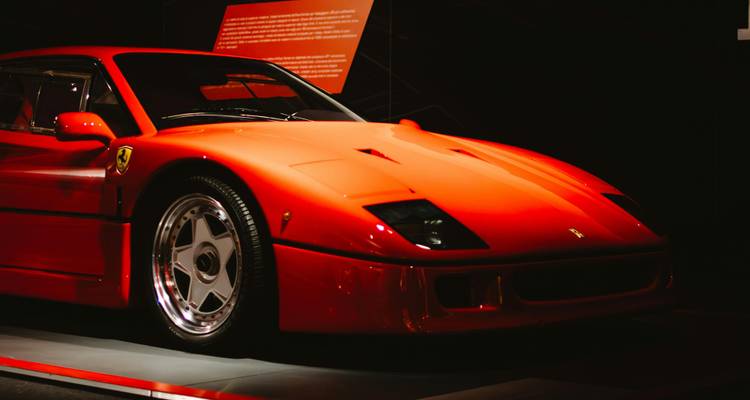 Iconische rode Ferrari F40 verlicht in een donkere tentoonstellingsruimte.