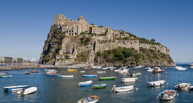 Das Aragonesische Schloss erhebt sich auf einer felsigen Insel, während farbenfrohe Boote auf dem blauen Meer treiben.