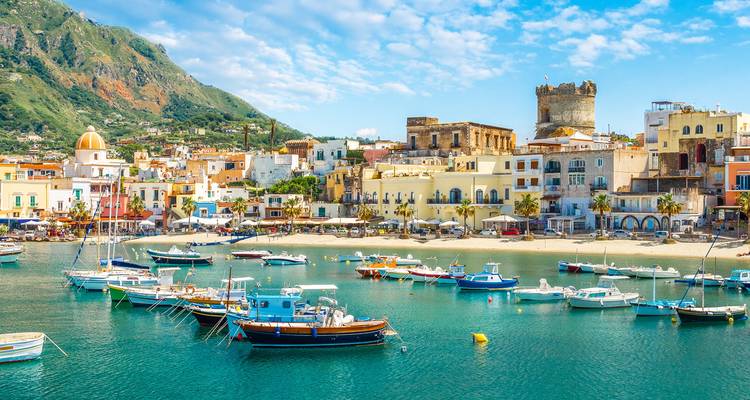 Lebendiger Hafen von Ischia mit pastellfarbenen Häusern, Fischerbooten und einem runden Wachturm vor grünen Hügeln.