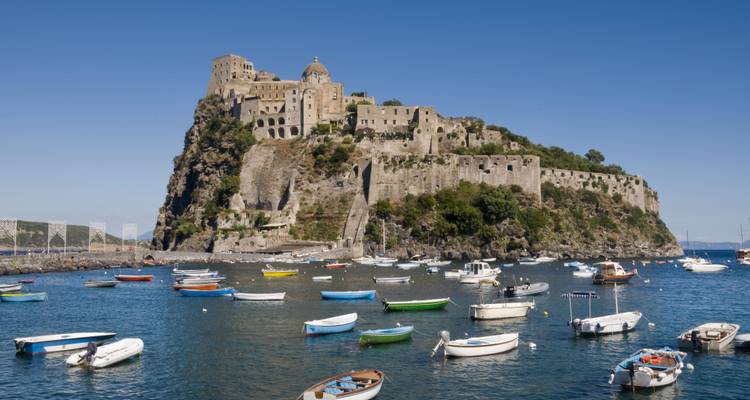 Majestic Aragonese Castle on rocky islet surrounded by small boats and deep blue water.