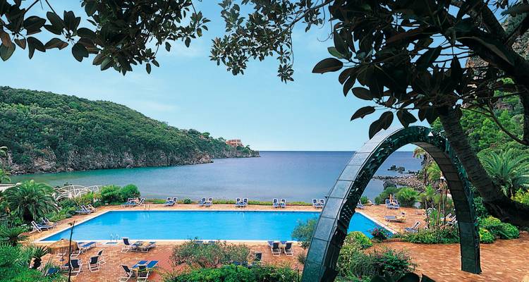 Scenic hotel pool framed by greenery overlooking a tranquil bay and forested cliffs.