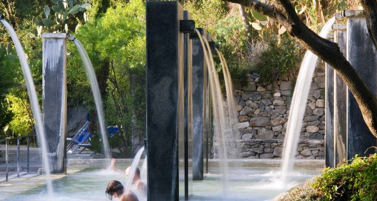Visitor relaxes under arching thermal water jets in an outdoor stone spa pool.