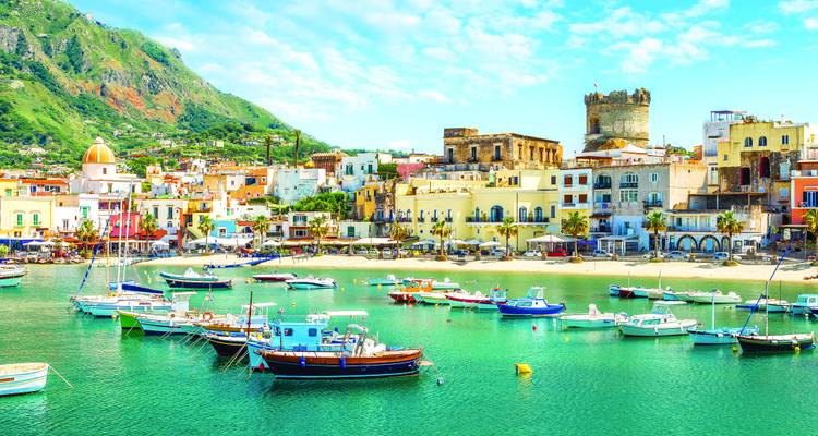 Colorful seaside village with domed church and boats floating on vivid emerald water.