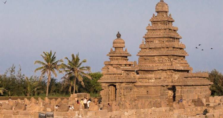 The ancient Shore Temple in Mahabalipuram rises above palm trees with small groups of visitors nearby.