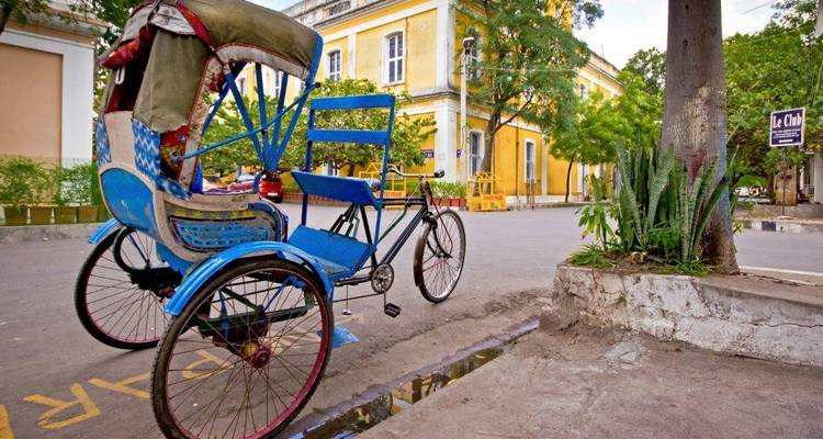 A colorful cycle rickshaw waits on a quiet colonial street lined with yellow heritage buildings in Puducherry.