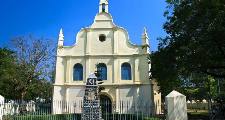 St. Francis Church in Fort Kochi stands pristine under a deep blue sky behind a historic stone cross.