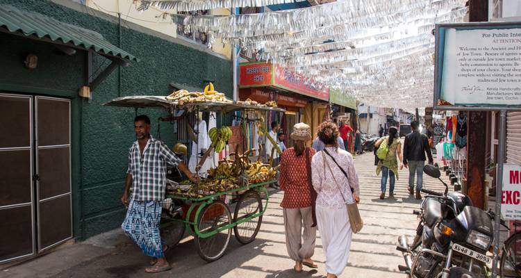 A street vendor sells bananas from a cart along a narrow market lane decorated with white streamers in Kochi.