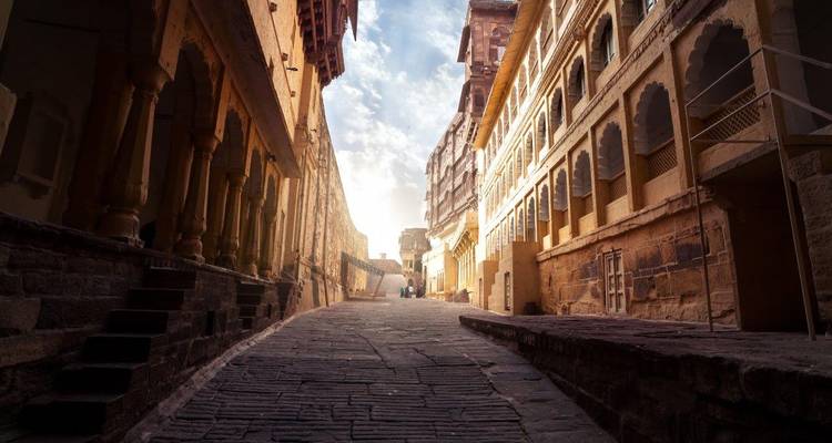 Sunlit narrow stone alleyway between ancient sandstone buildings in Rajasthan.