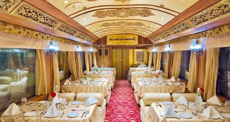 Elegant dining car of the Palace on Wheels set with white linens, chandeliers and picture windows.