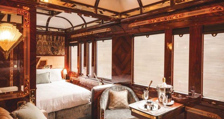 Sumptuous private suite on board the luxury train with wood paneling, four-poster bed and champagne service.