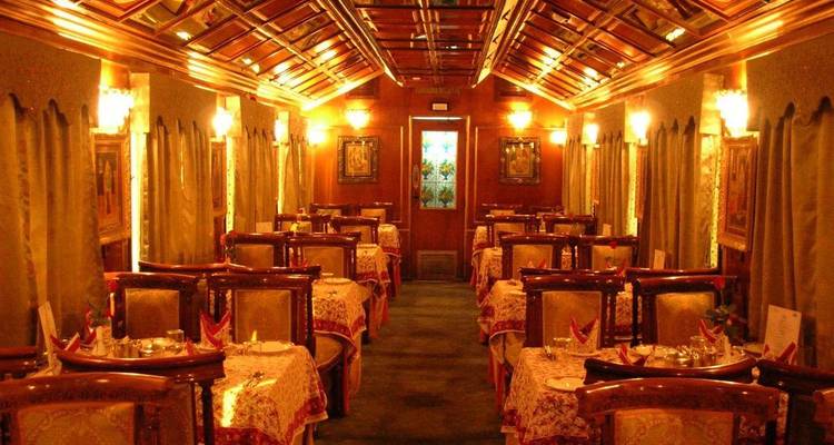 Warmly lit vintage dining carriage with richly patterned tablecloths and wooden ceiling on a heritage train.