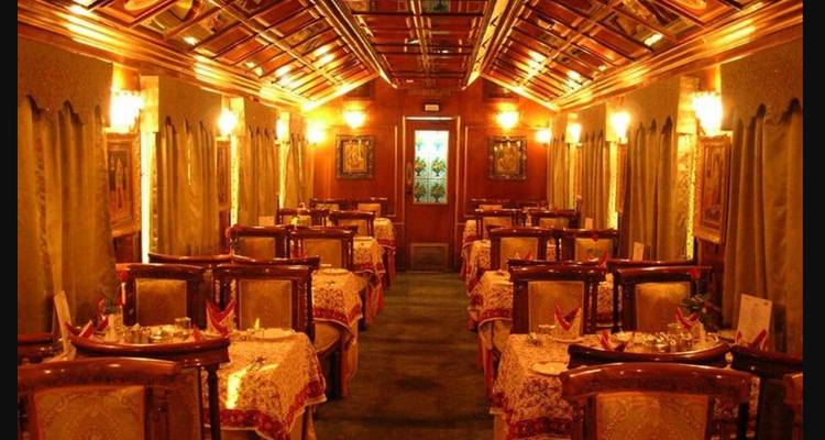 Elegant dining carriage with ornate ceiling panels, soft lighting and formally set tables