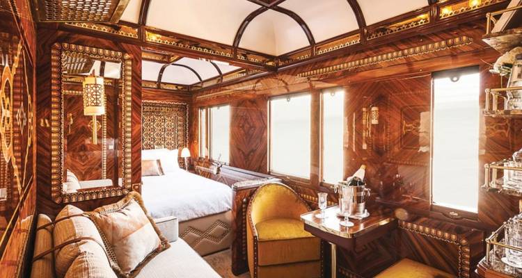 Luxurious private train suite with inlaid wood panels, plush seating and a made-up double bed