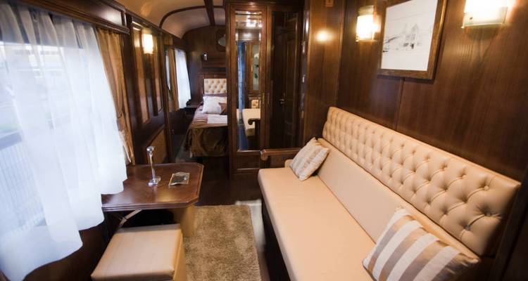 Elegant wood-panelled train cabin with cream sofa, window drapes and soft lighting