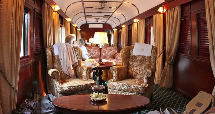Classic lounge carriage with patterned armchairs and couples enjoying tea under warm lamps