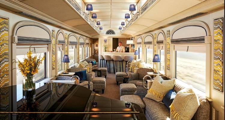 Bright bar lounge rail car with grand piano, arched windows and plush seating lit by lamps