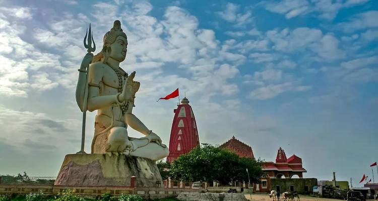 Huge white statue of Lord Shiva beside the Nageshwar Jyotirlinga temple under a partly cloudy sky in Dwarka.