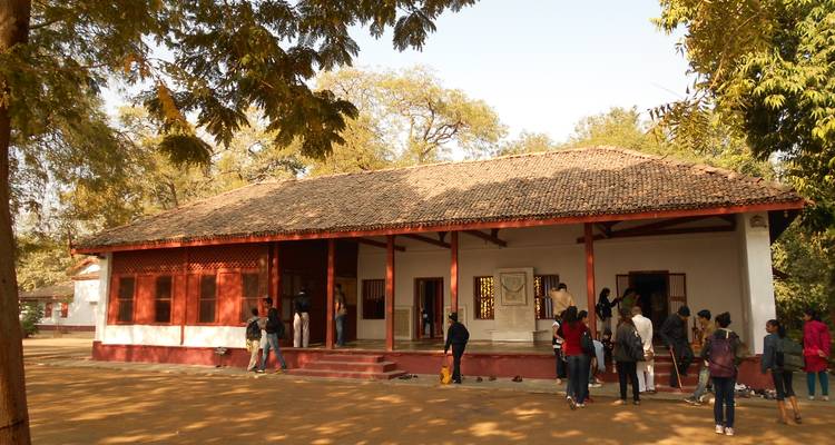 Visitors gather outside the simple white bungalow at Sabarmati Ashram surrounded by trees.