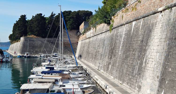 Los barcos se amarran junto a altas fortificaciones de piedra que bordean una tranquila marina.
