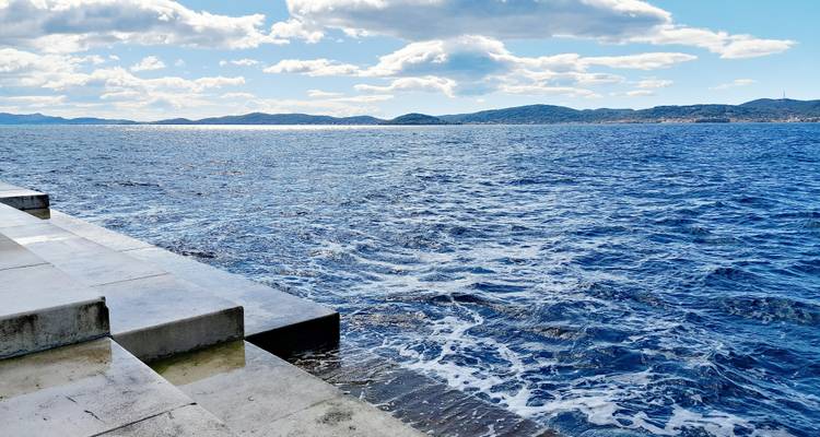 Los pasos de hormigón del órgano marino de Zadar se encuentran con olas de cobalto agitadas bajo nubes dispersas.