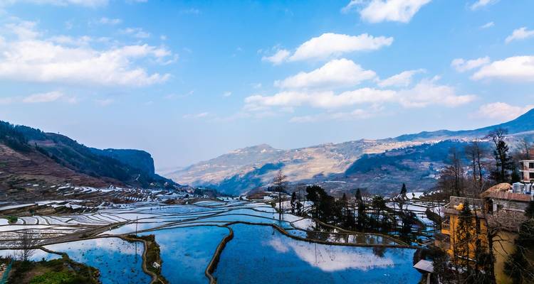 Extensas terrazas de arroz escalonadas llenas de agua que reflejan el cielo azul y las colinas