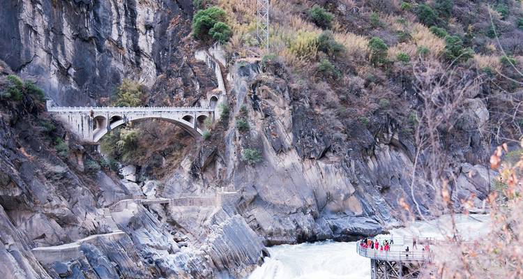 Garganta estrecha con un puente de piedra que atraviesa un río caudaloso y visitantes en una plataforma de observación