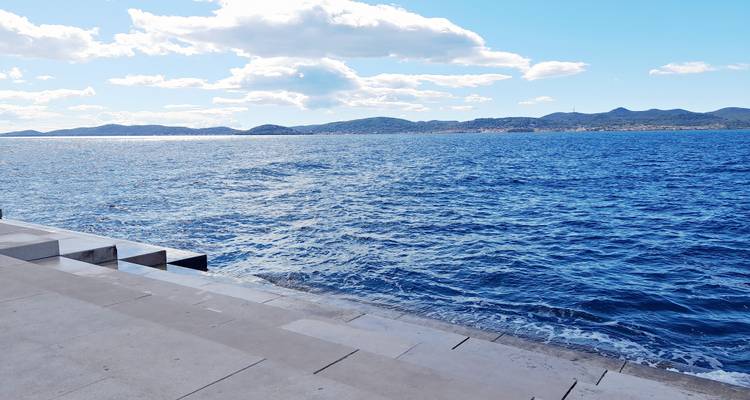 Modern stone steps of a seaside promenade meeting deep blue Adriatic waters with distant islands.