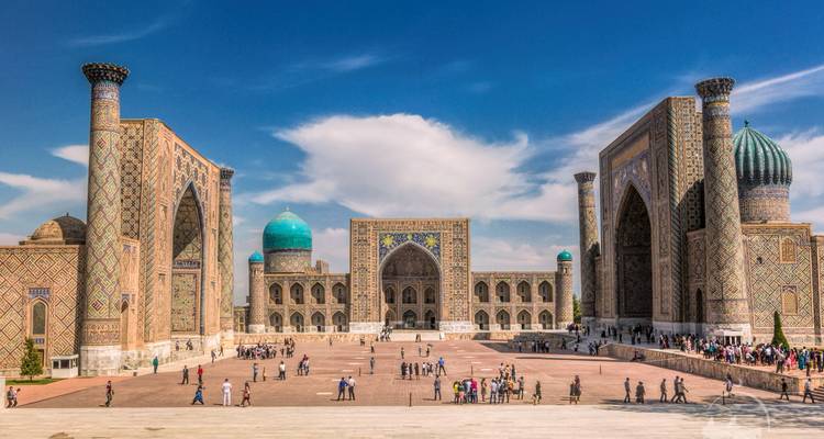 Panoramic view of Registan Square with ornate madrasas and turquoise domes under blue sky.