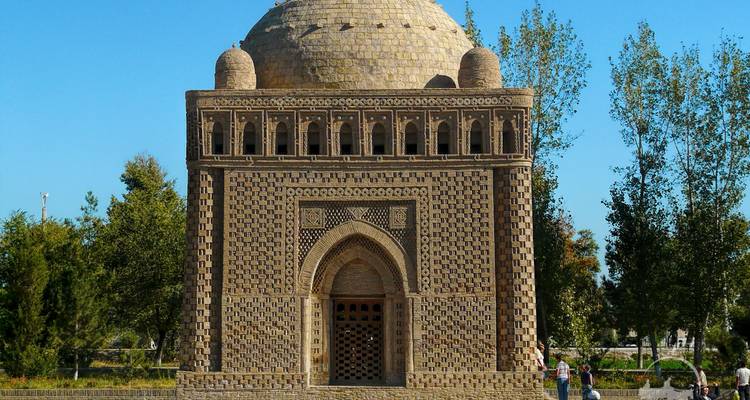 Domed brick mausoleum with intricate geometric patterns set in a park.