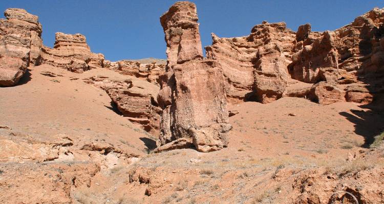 Eroded red rock formations and columns in a dry canyon landscape under clear sky.